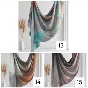 May include: Three different patterned scarves in shades of gray, brown, and teal. The scarves are draped over a white surface with a white vase and dried flowers in the background. The numbers 13, 14, and 15 are visible in the image.
