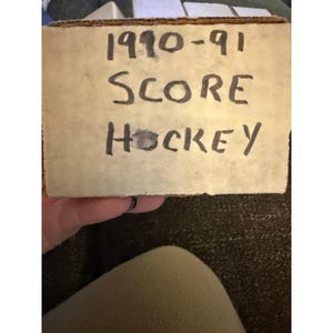 May include: A cardboard box with the handwritten text "1990-91 SCORE HOCKEY". The box is a light tan color and appears to be vintage. The text is written in black marker.