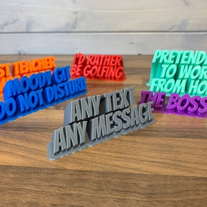 Peut inclure: Cinq pancartes imprimées en 3D avec des messages différents. Les pancartes sont de différentes couleurs, notamment orange, bleu, rouge, gris, vert et violet. Les messages sur les pancartes sont : "Best Teacher", "Moody Git Do Not Disturb", "I'd Rather Be Golfing", "Any Text Any Message", "Pretending To Work From Home The Boss".