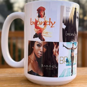 May include: White ceramic mug featuring multiple images of Brandy, including album art and the singer's name. The mug has a large handle and is displayed on a wooden surface.