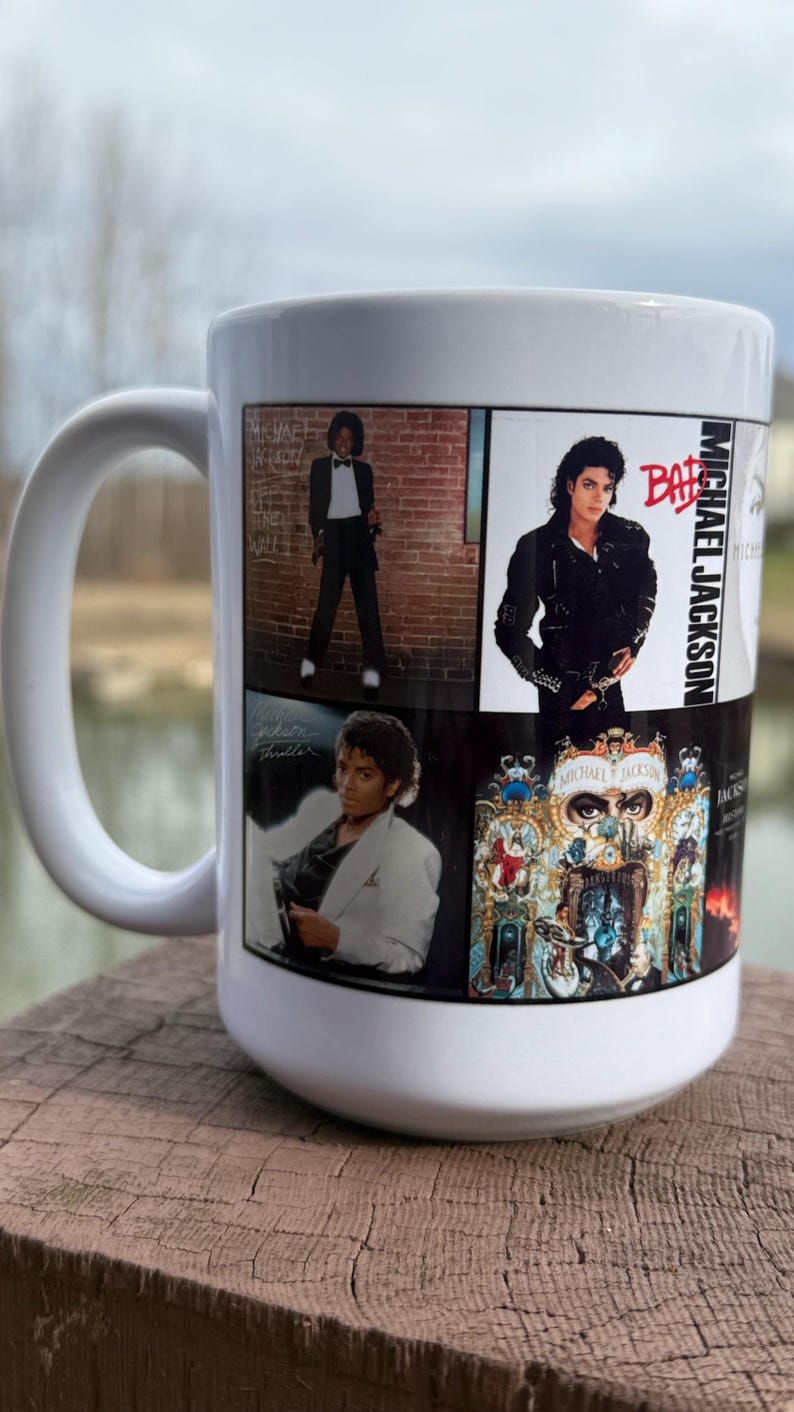 May include: White ceramic mug featuring multiple images of Michael Jackson, including album art and iconic poses. The mug has a large handle and is displayed on a wooden surface.