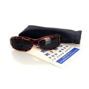 May include: Brown tortoise shell pinhole glasses with black lenses and a black fabric case. The glasses are on a white surface with a blue and white card that says "Everything you need to know about original pinhole glasses".