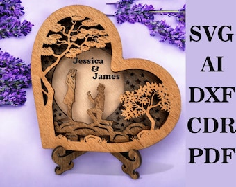 May include: A wooden heart-shaped box with a cutout design of a couple proposing under a moon and stars. The box has a stand and is personalized with the names "Jessica & James".