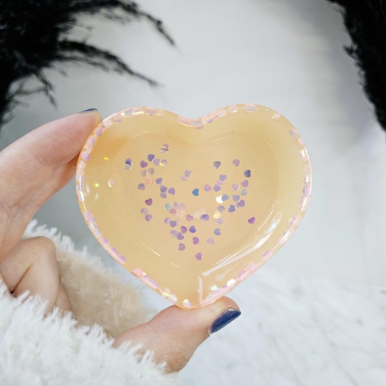 May include: A heart-shaped dish made of clear resin with a light peach colour and iridescent pink and purple glitter hearts.