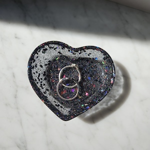 May include: A black heart-shaped trinket dish with iridescent glitter and two silver rings inside.