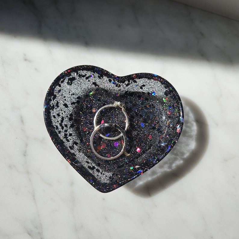 May include: A black heart-shaped trinket dish with iridescent glitter and two silver rings inside.