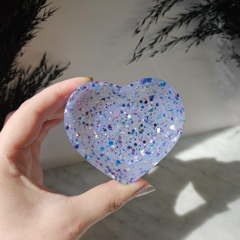 May include: A heart-shaped dish made of clear resin with blue, pink and white glitter embedded throughout.