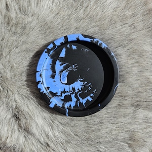 May include: A round, black and blue decorative tray. The tray has a circular design with a black center and a blue and black marbled pattern around the edge. The tray is made of a solid material.