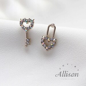 May include: A pair of silver-coloured earrings. One is a key shape, the other a heart-shaped lock. Both are encrusted with iridescent crystals. The earrings are set against a white background. The brand name "Allison Jewelry" is at the bottom.