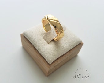May include: A gold ring with a textured, geometric design. The ring is displayed on a small, wooden box with a white lining.