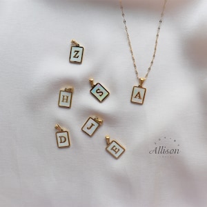 May include: A set of gold-tone initial pendants with white enamel and gold lettering. The letters are A, D, E, H, J, S, and Z. The pendants are on a white surface. The word "Allison" is printed in the bottom right corner of the image.