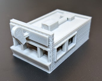 May include: A gray 3D printed model of a small building with a sign that says "K&B". The building has a flat roof and windows on the front and side.