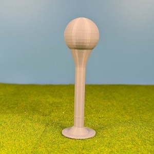 May include: A gray 3D printed water tower model with a round top and a tall, slender base. The model is sitting on a green surface.