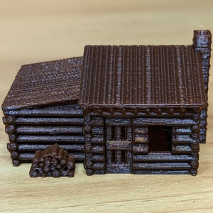 Peut inclure: Une petite cabane en rondins de bois brune avec une cheminée et une fenêtre. La cabane est faite de rondins et a un toit en bardeaux. Il y a une pile de rondins devant la cabane.