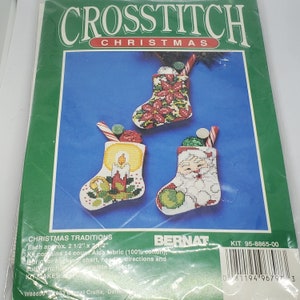 May include: A cross stitch kit for making three Christmas stockings. The stockings are 2 1/2 inches by 3 1/2 inches and feature a poinsettia, a candle, and Santa Claus. The kit includes 14 count Aida fabric, embroidery floss, a needle, a chart, and instructions. The kit is made by Bernat Crafts and the kit number is 95-8865-00.