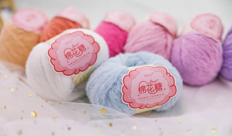 Puede incluir: Surtido de ovillos de lana de colores con una etiqueta rosa que dice "Sweet  棉花糖" en caracteres chinos. La lana es suave y esponjosa, perfecta para tejer o hacer ganchillo.