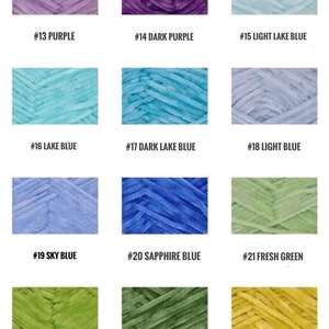 May include: A color chart of yarn samples in various shades of purple, blue, green, and yellow. The yarn is a fuzzy, textured type. Each sample is labeled with a number and color name.