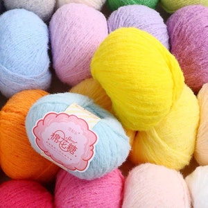 Puede incluir: Una variedad de ovillos de lana de colores en tonos de azul, rosa, amarillo, naranja y blanco. La lana es suave y esponjosa, y los ovillos est&aacute;n dispuestos en una pila. La etiqueta en uno de los ovillos dice "Sweet Cotton."