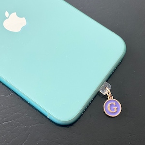 May include: A light blue iPhone with a white Apple logo. A small gold charm with a purple letter G is attached to the bottom of the phone.