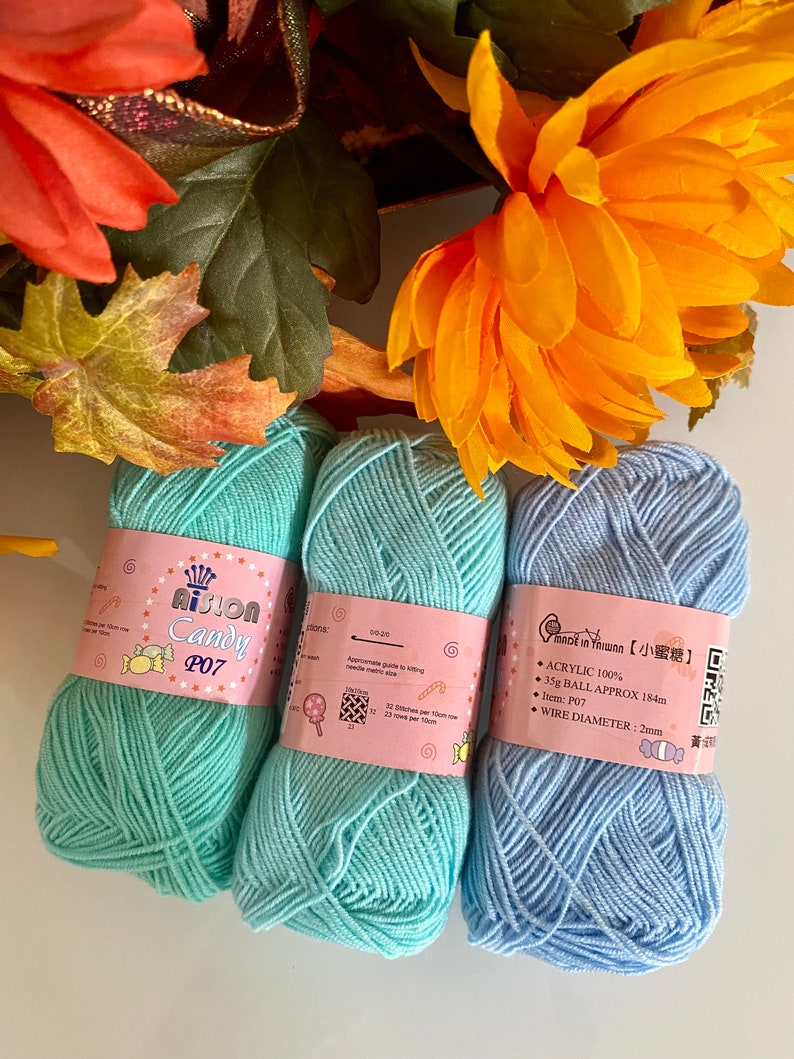 Puede incluir: Tres ovillos de lana, uno azul claro, dos turquesa, con etiquetas que dicen "AiSton Candy P07" y "Made in Taiwan 小蜜糖". Las etiquetas también incluyen detalles como "Acrílico 100%", "35g Ball Approx 184m", "Diámetro del alambre: 2mm" y un código QR.
