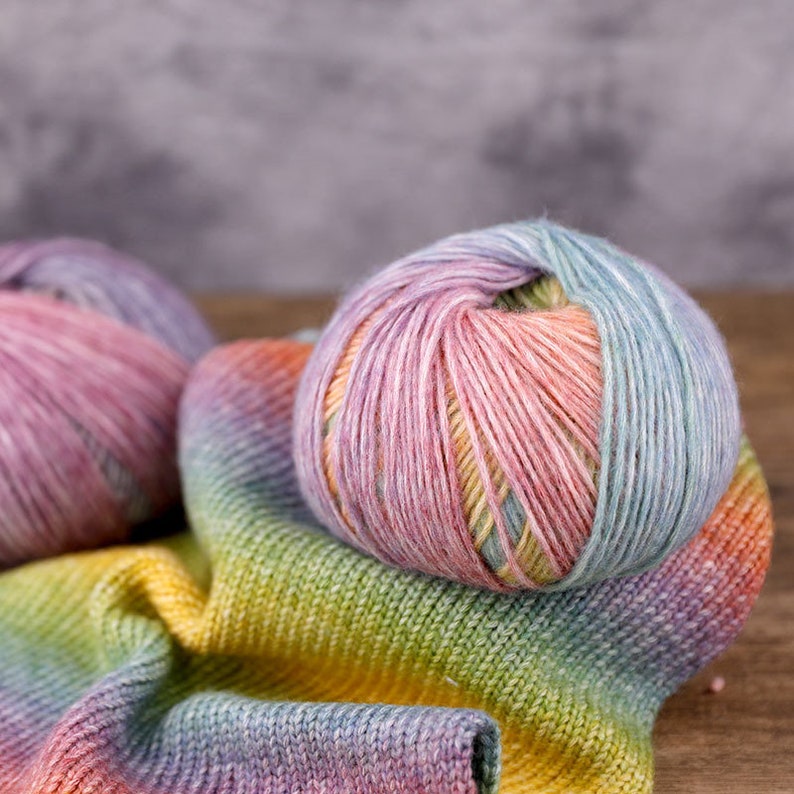 Rainbow variegated yarn cakes resting on top of a knitted fabric.