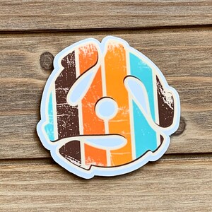 May include: A vintage-style vinyl record sticker with a distressed look. The sticker features a brown, orange, and blue striped design.