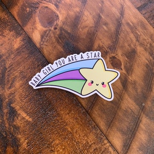 May include: A yellow star with a smiling face, with a rainbow tail and the text "BABY GIRL YOU ARE A STAR" in black.