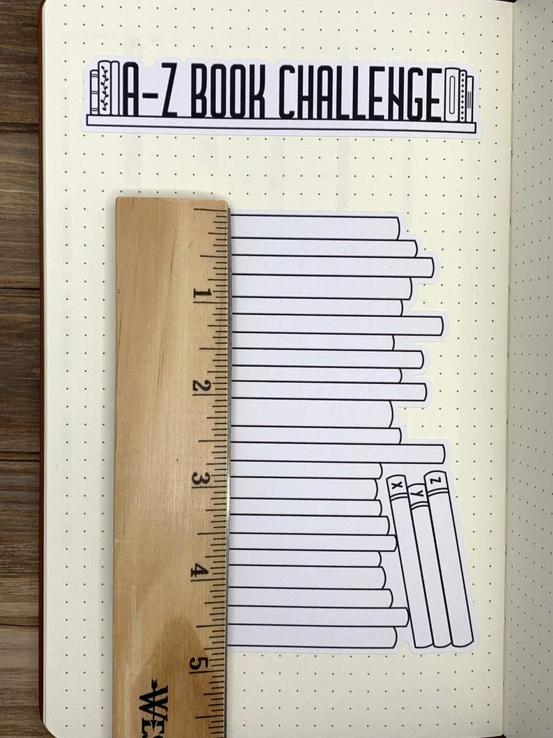 May include: A-Z Book Challenge sticker with a stack of books, a ruler, and a dotted notebook page. The sticker shows a stack of books with the letters X, Y, and Z on the spines of the last three books.
