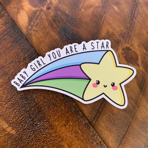 May include: A yellow star with a smiling face, with a blue, green, and purple shooting star tail. The text "BABY GIRL YOU ARE A STAR" is written on the tail.