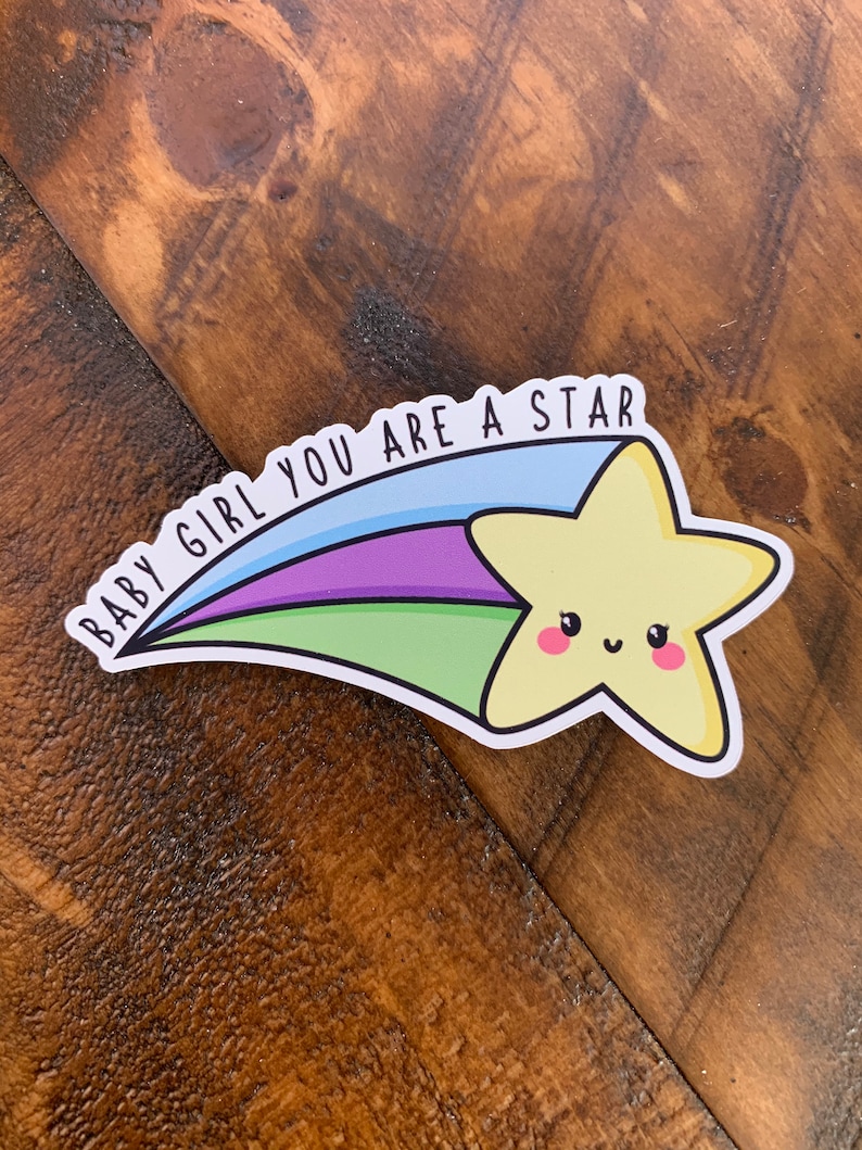 May include: A yellow star with a smiling face, with a blue, green, and purple shooting star tail. The text "BABY GIRL YOU ARE A STAR" is written on the tail.