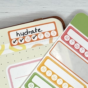 K&ouml;nnte beinhalten: Ein Satz farbenfroher w&ouml;chentlicher Gewohnheitstracker-Aufkleber mit dem Text "hydrate" und Kontrollk&auml;stchen f&uuml;r jeden Tag der Woche. Die Aufkleber sind f&uuml;r die Verwendung in einem Planer oder Tagebuch gedacht.