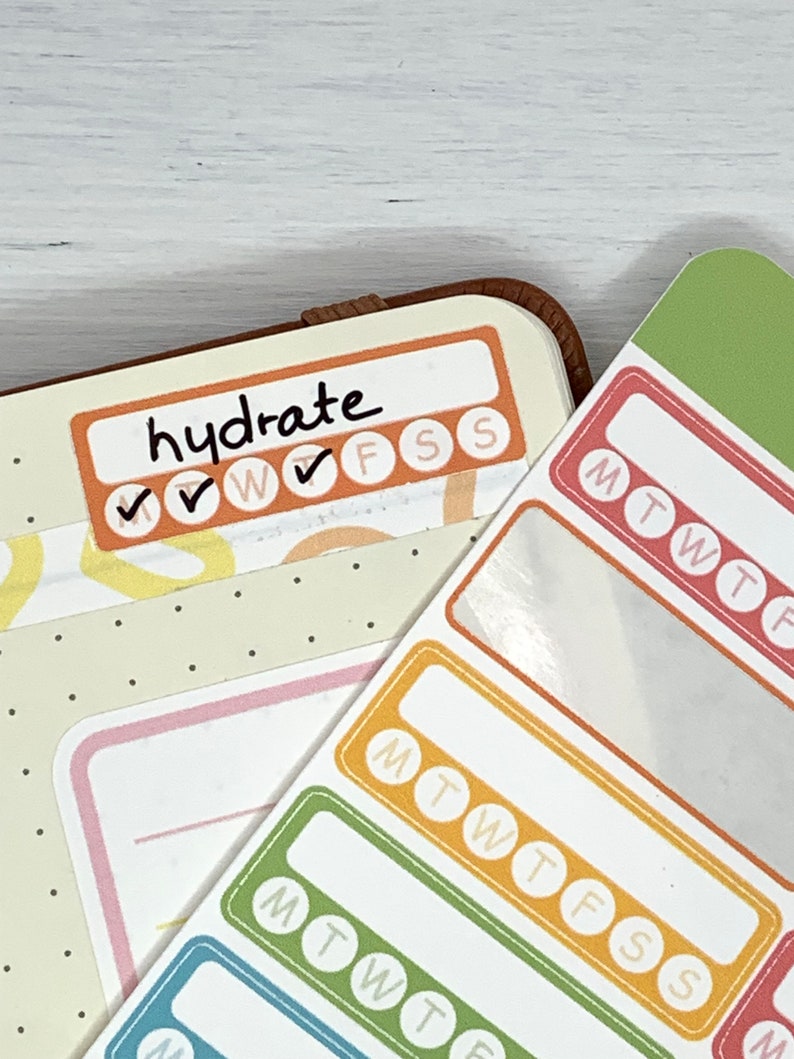K&ouml;nnte beinhalten: Ein Satz farbenfroher w&ouml;chentlicher Gewohnheitstracker-Aufkleber mit dem Text "hydrate" und Kontrollk&auml;stchen f&uuml;r jeden Tag der Woche. Die Aufkleber sind f&uuml;r die Verwendung in einem Planer oder Tagebuch gedacht.