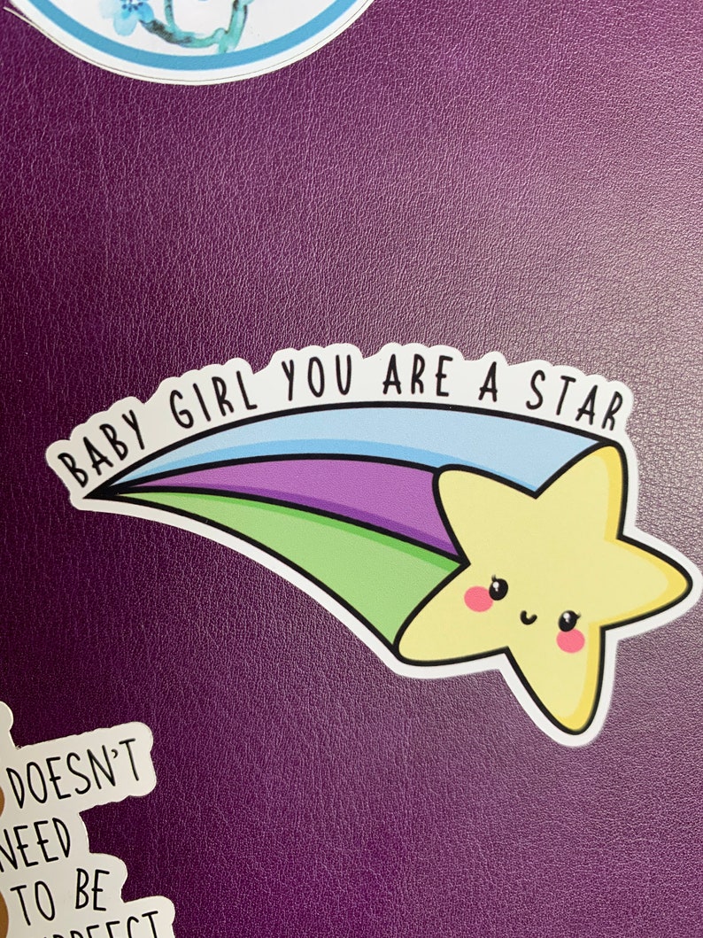 May include: A yellow star with a smiling face, on a blue, green, purple and white shooting star with the text "Baby Girl You Are A Star".