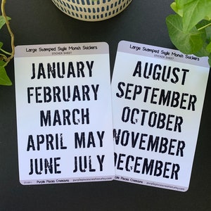 May include: Two sticker sheets with black stamped month names on a white background. The first sheet has January, February, March, April, May, June, and July. The second sheet has August, September, October, November, December. The sheets are labeled "Large Stamped Style Month Stickers".