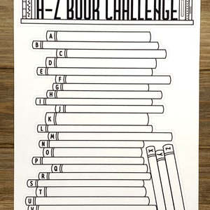 May include: A-Z Book Challenge sticker sheet with 26 blank book spines for a reading challenge. The sticker sheet features a black and white illustration of a bookshelf with books labeled A-Z.