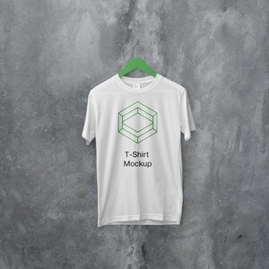 May include: White t-shirt mockup hanging on a green hanger against a gray concrete wall. The t-shirt has a geometric design and the text "T-Shirt Mockup" printed on the front.