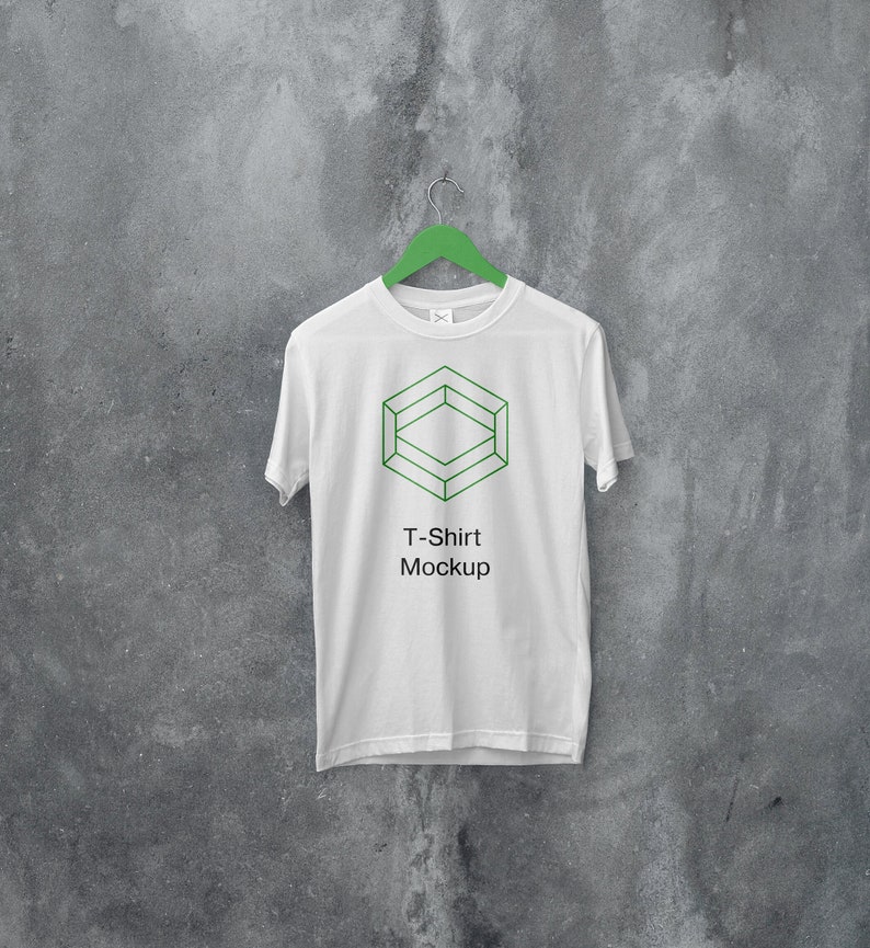 May include: White t-shirt mockup hanging on a green hanger against a gray concrete wall. The t-shirt has a geometric design and the text "T-Shirt Mockup" printed on the front.