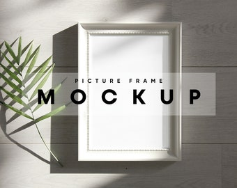 May include: White picture frame mockup on a light wood background with a green leaf and shadow. The text "PICTURE FRAME MOCKUP" is visible on the frame.