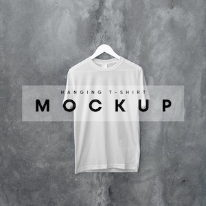 May include: White t-shirt hanging on a hanger against a gray concrete wall. The text "HANGING T-SHIRT MOCKUP" is printed on a white rectangle in front of the shirt.