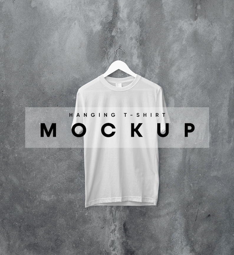 May include: White t-shirt hanging on a hanger against a gray concrete wall. The text "HANGING T-SHIRT MOCKUP" is printed on a white rectangle in front of the shirt.