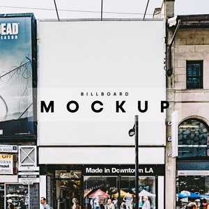 May include: A white billboard mockup with the text "BILLBOARD MOCKUP" in black letters. The billboard is located in a city setting with shops and pedestrians in the foreground.