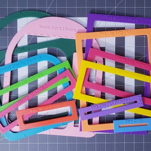 Puede incluir: Un conjunto de plantillas de plástico de colores para coser bolsos. Las plantillas están etiquetadas con nombres como "Bolsillo frontal con cremallera", "Paneles principales de cremallera", "Anclaje de correa", "Extensión trasera y forros", "Bolsillo interior deslizante", "Bolsillo deslizante frontal con cremallera", "Asa de transporte", "Godet de bolsillo frontal con cremallera" y "Clip para llaves".
