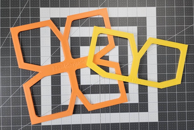 May include: Two plastic stencils, one orange and one yellow, with geometric shapes. The orange stencil has the text "Rowicozy" on it, and the yellow stencil has the text "Fold 101b" on it.