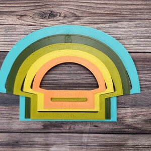May include: Set of five nesting half-circle stencils in turquoise, green, yellow, orange, and light orange. The stencils are made of plastic and have a smooth, glossy finish.