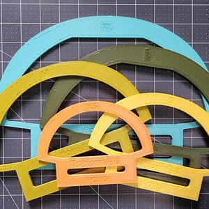 May include: Five different sized, semi-circular plastic templates in various colors, including turquoise, yellow, orange, and green. The templates are labeled with sizes XS, S, M, L, and XL.