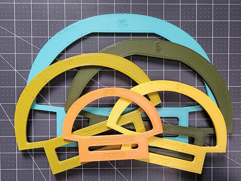 May include: Five different sized, semi-circular plastic templates in various colors, including turquoise, yellow, orange, and green. The templates are labeled with sizes XS, S, M, L, and XL.