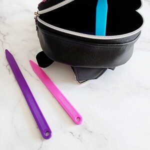 May include: A black zippered bag with a purple and blue design. The bag is open and there are two colorful straps inside. The straps are purple and pink.