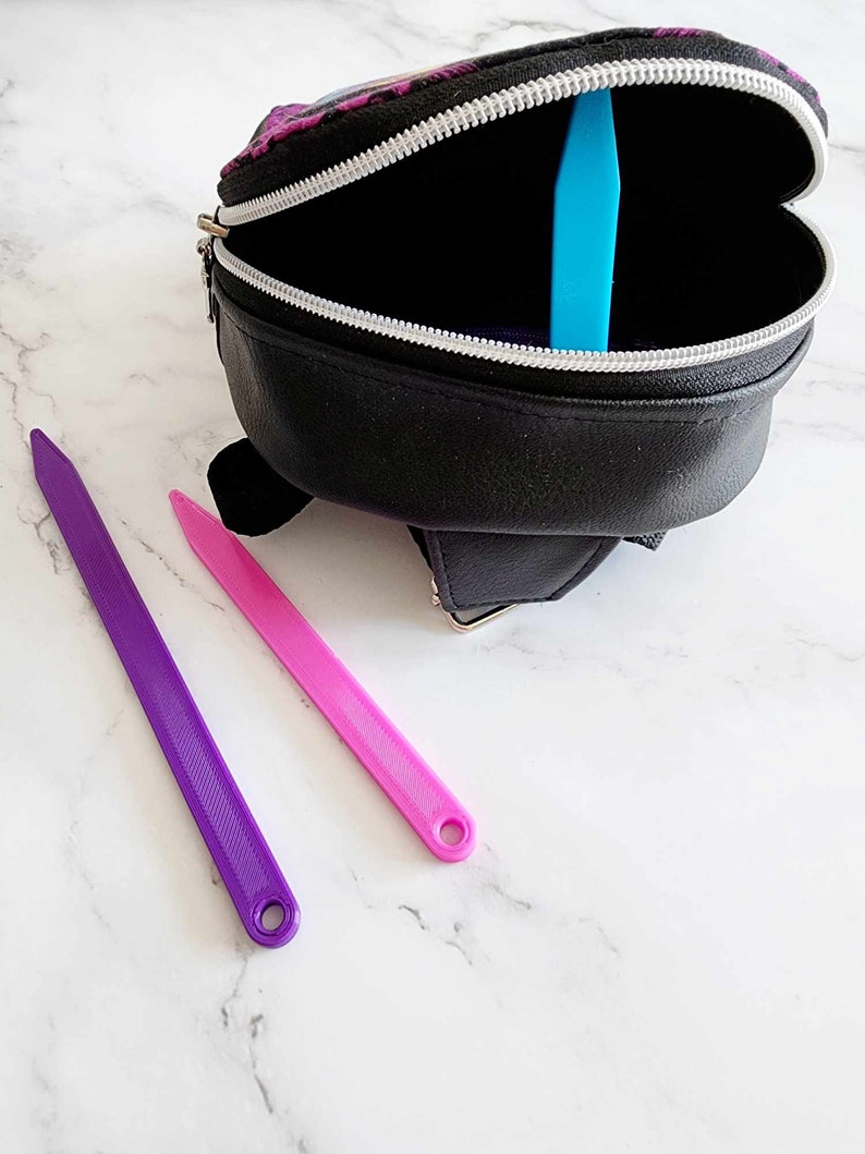 May include: A black zippered bag with a purple and blue design. The bag is open and there are two colorful straps inside. The straps are purple and pink.