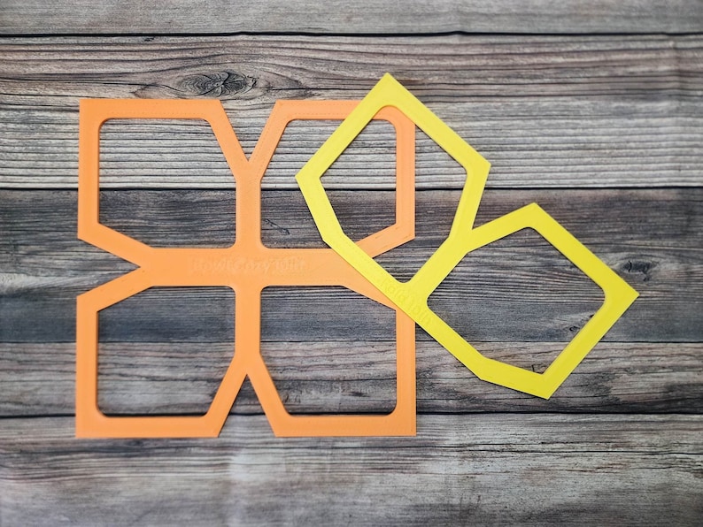 May include: Two geometric shapes, one orange and one yellow, are arranged on a wooden surface. The orange shape is a larger, more complex design with multiple points. The yellow shape is a smaller, simpler design with fewer points.
