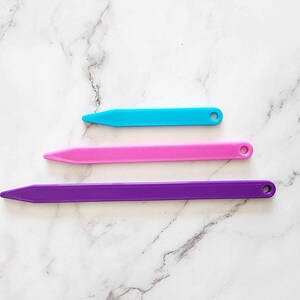 May include: Three plastic knitting needles in different sizes. The needles are purple, pink, and blue.